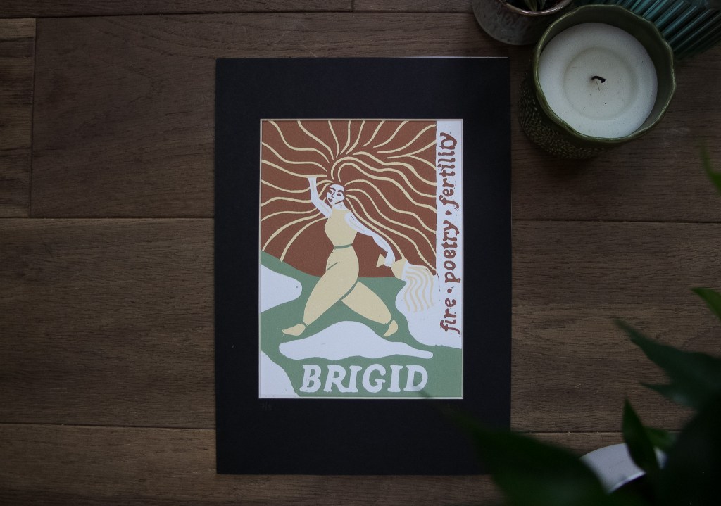 A linocut print of Goddess Brigid, depicted with flowing hair and arms raised, surrounded by radiant lines symbolizing fire and inspiration. The words 'fire, poetry, fertility' are incorporated into the design, with 'BRIGID' prominently displayed at the bottom.