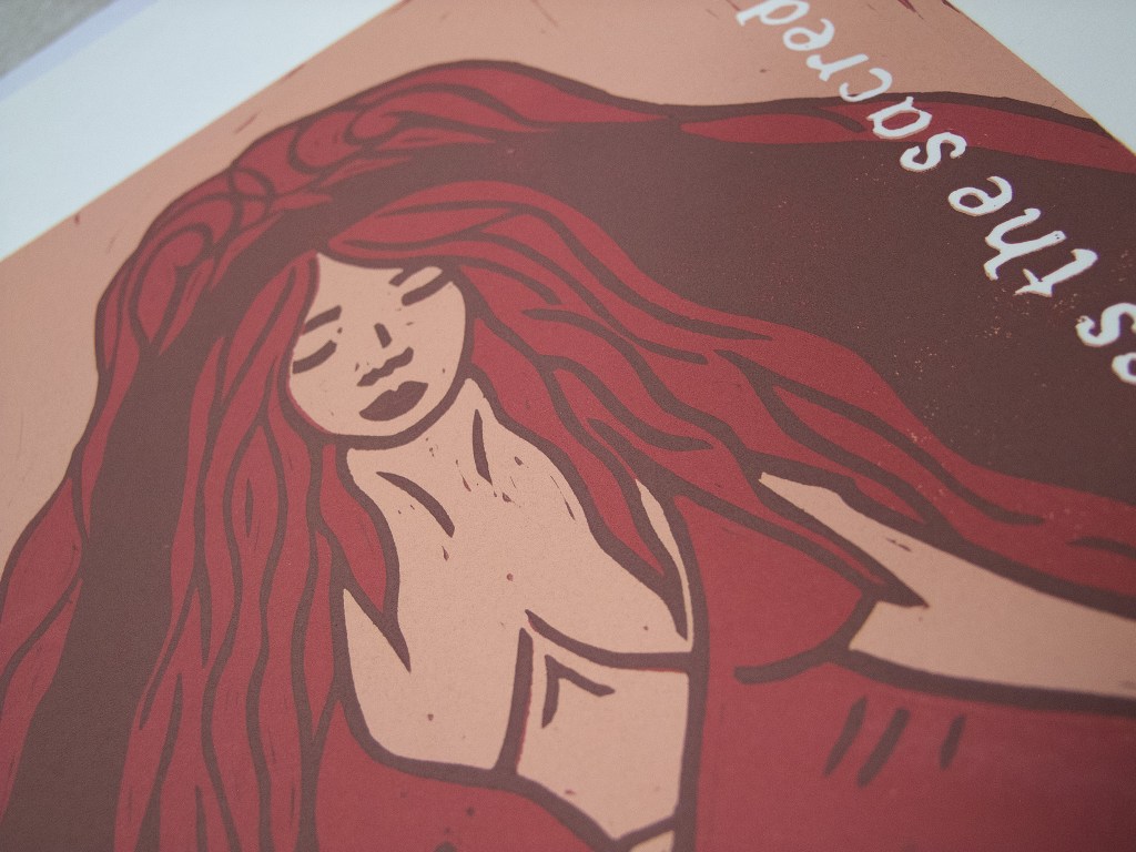 A linocut print depicting a goddess with flowing red hair and a serene expression, representing the element of fire.