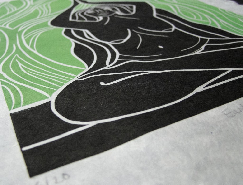A close-up of a linocut art piece featuring an abstract depiction of a female figure with flowing hair, outlined in white against a green and black background, emphasizing themes of earth and nature.