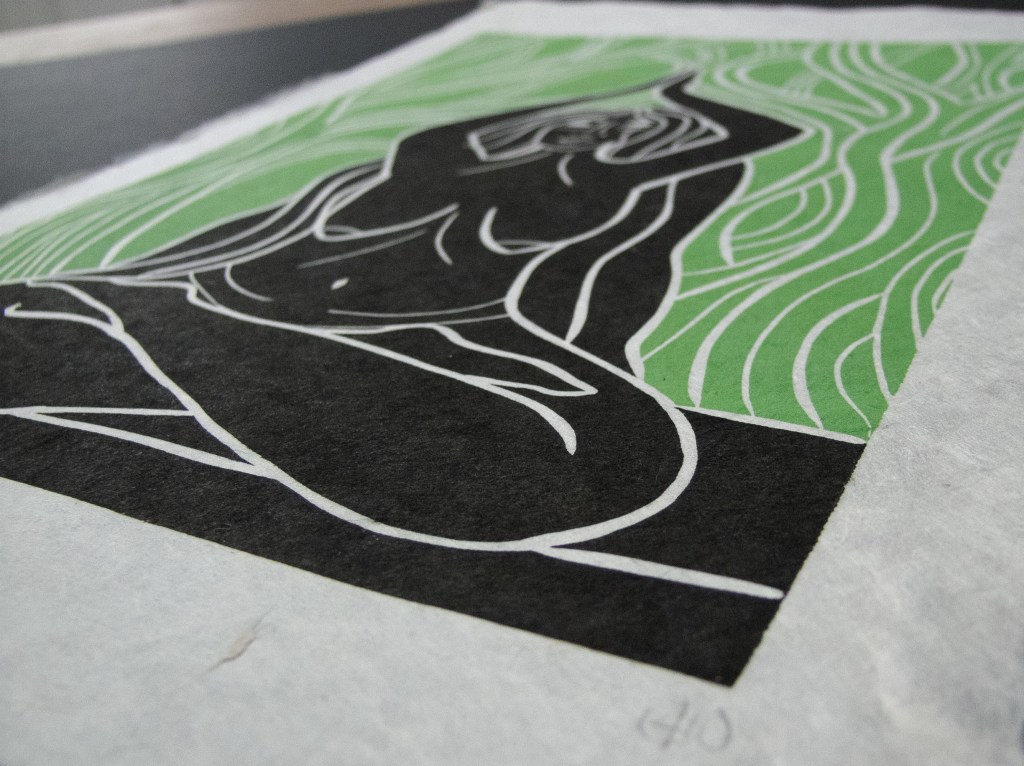 A linocut print depicting a nude female figure in a seated position, surrounded by flowing green patterns, symbolizing earth and nature.
