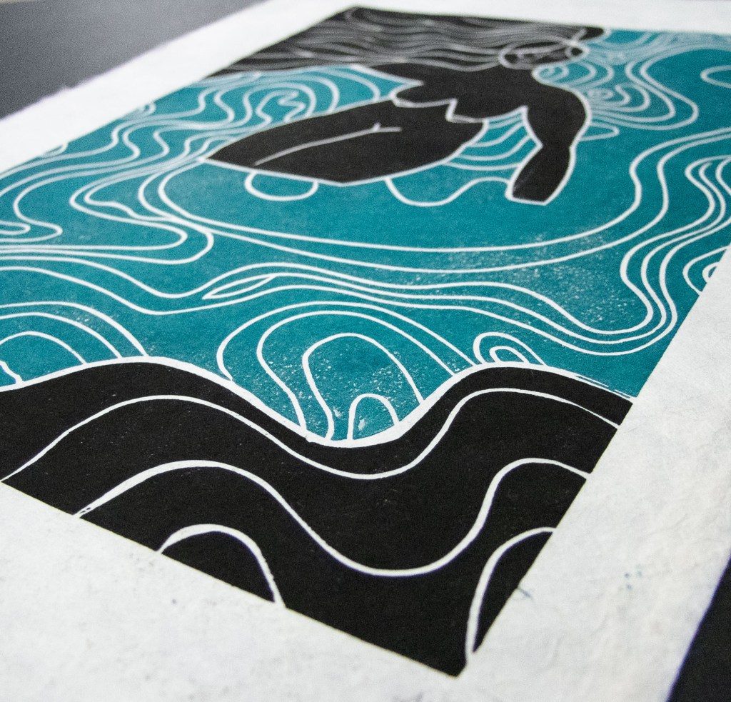 A linocut print depicting a stylized figure of a woman swimming in waves, surrounded by intricate line patterns representing water.