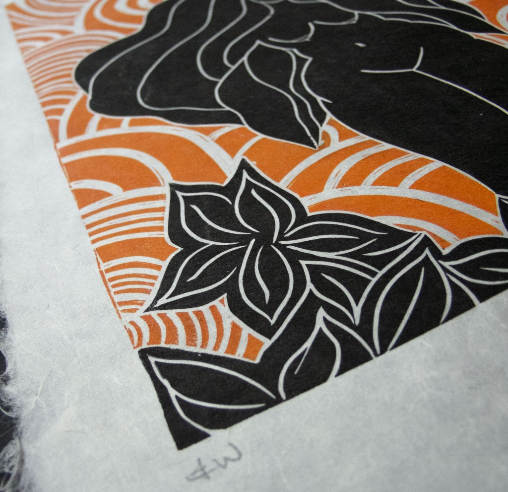 A linocut print featuring a stylized representation of a goddess with flowing hair, surrounded by organic shapes and swirling patterns in black and orange.