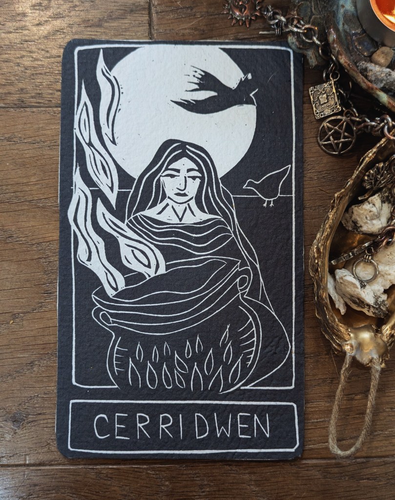 A linocut print of Cerridwen, the goddess, featuring a woman with flowing hair and a cauldron, surrounded by flames and birds against a circular moon backdrop.